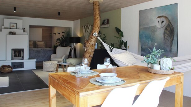 A dining area with a wooden table set for two, a hammock, and a painting of an owl on the wall. - Eulenschlupf, modern and lovely vacation apartment with garden and sauna (Ühlingen-Birkendorf)