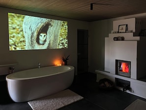 Ein modernes Badezimmer mit einer freistehenden Badewanne, einem Kamin und einem großen Bildschirm, der eine Eule zeigt.
