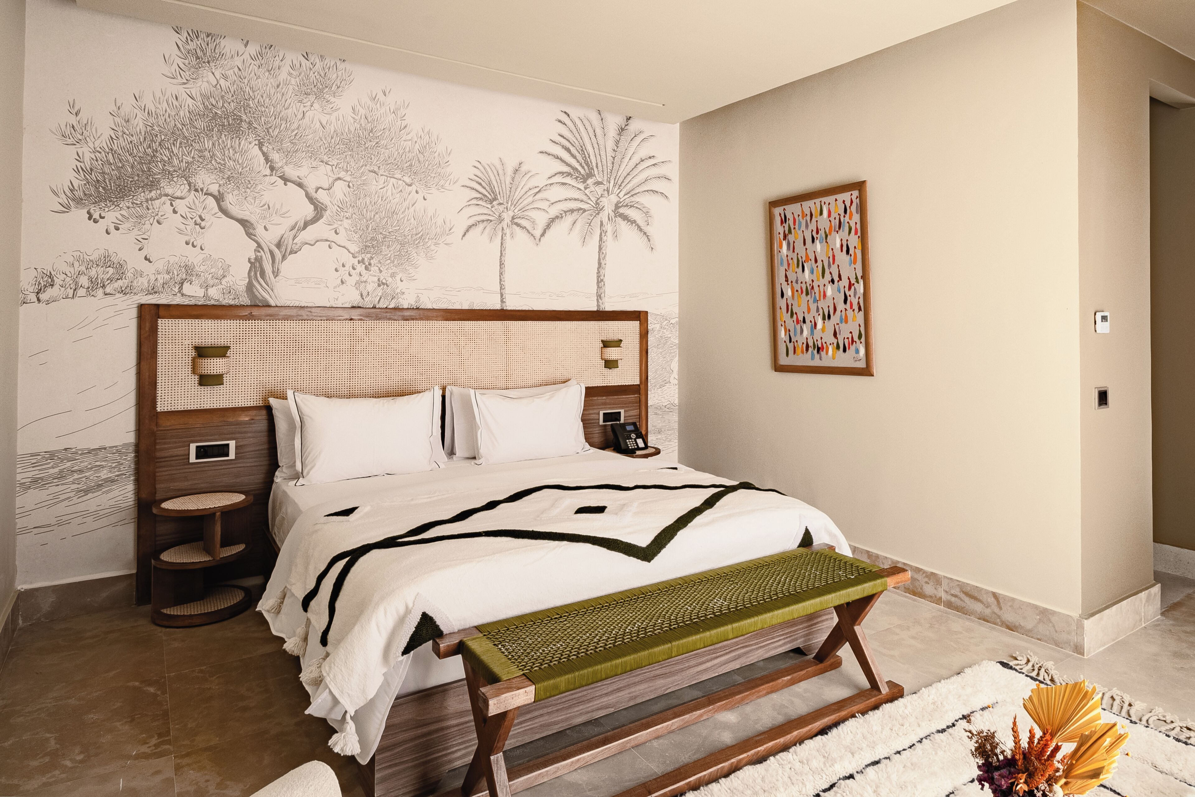 A bedroom with a large bed, a bedside table, a wall-mounted phone, a small cat tree, and a decorative wall art piece.