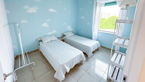 Ein Zimmer mit zwei Einzelbetten, einem Fenster mit Blick, einer weißen Metallbettumrandung und einer weißen Lampe.