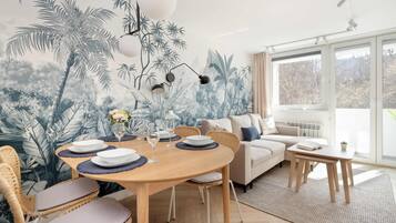 A dining area with a round wooden table, white plates, and glasses, surrounded by wicker chairs.