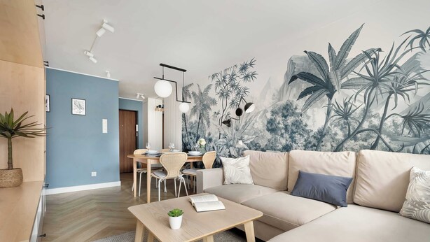 A modern living room with a large mural, a sofa, a dining table, and a coffee table. - Cozy Apartment with Balcony | Close to Beach and Station (Gdynia)