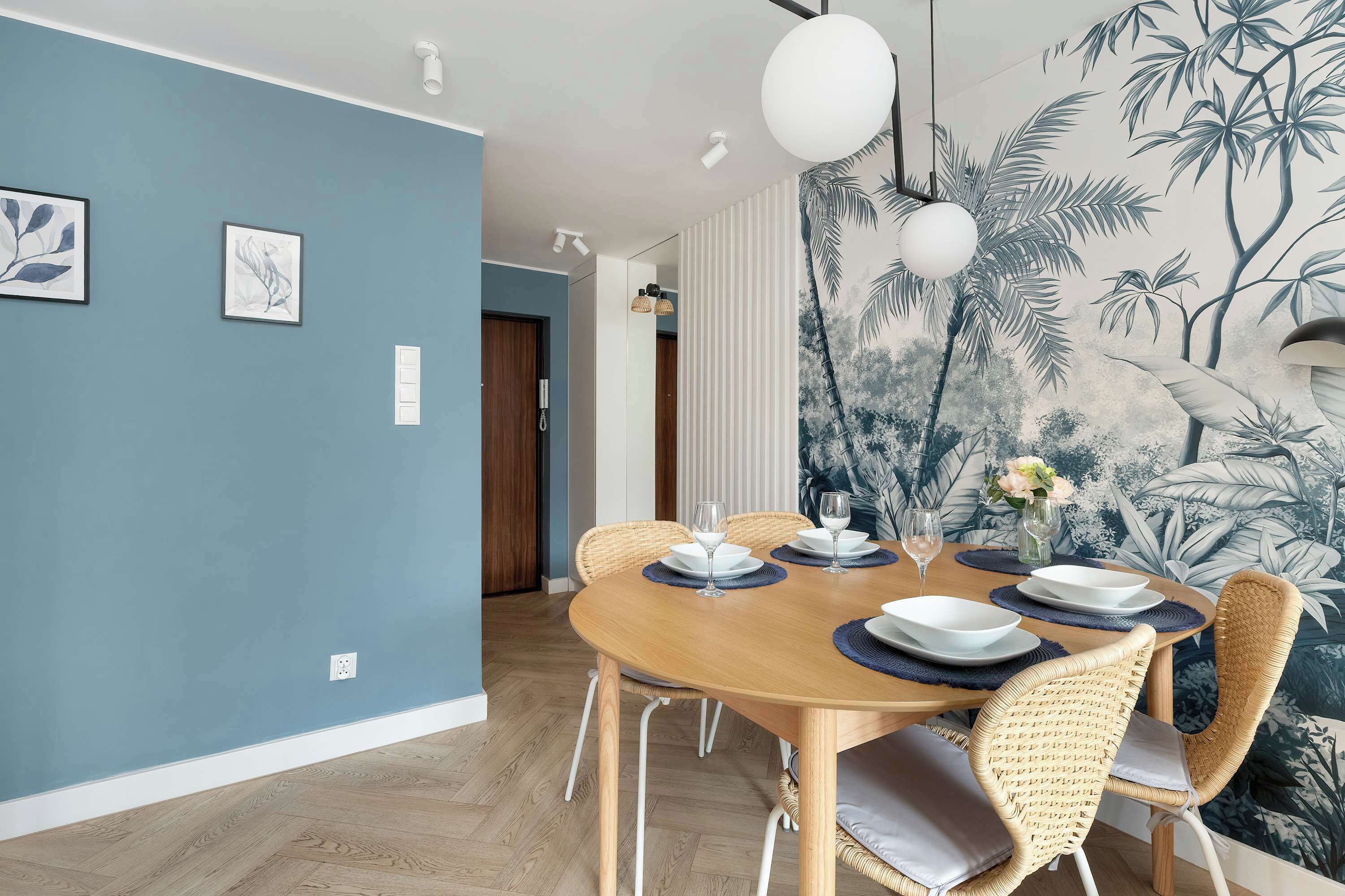 A dining area with a round wooden table set for four, surrounded by wicker chairs with cushions.