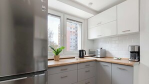 A modern kitchen with grey cabinets, a stainless steel refrigerator, and a window with a view of a building. - Cozy Apartment with Balcony | Close to Beach and Station (Gdynia)