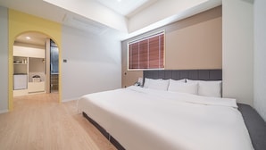 Une chambre d’hôtel avec un lit, une fenêtre avec des stores, une armoire et une salle de bain visible à travers une arche.