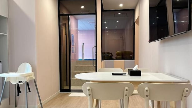 Une pièce moderne avec une table ronde, deux chaises, un téléviseur fixé au mur et une porte donnant sur une autre pièce.