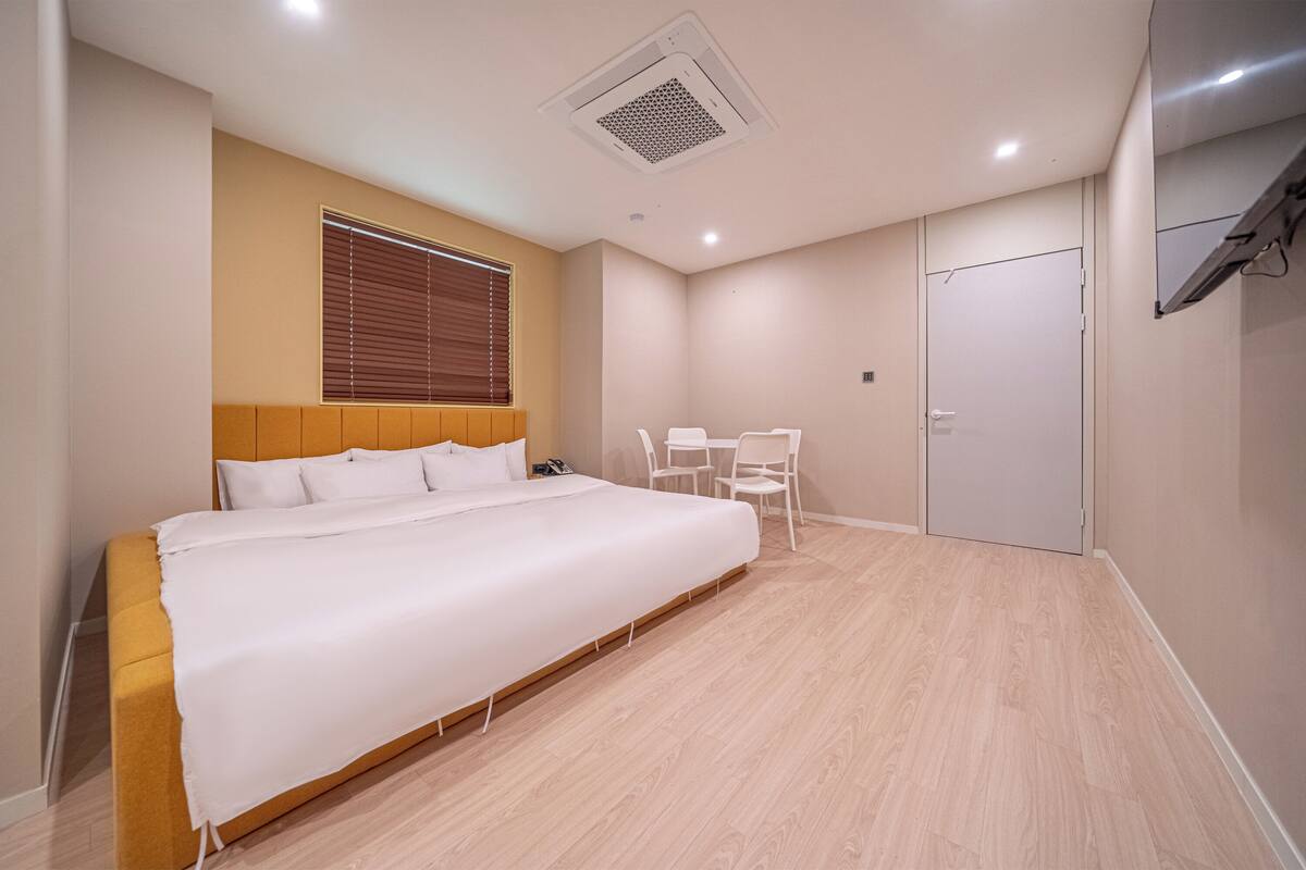 A bedroom with a bed, a desk, a chair, a wardrobe, and a window with blinds.