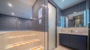 Une salle de bain moderne avec une porte en verre, un lavabo avec un miroir et un sol carrelé.