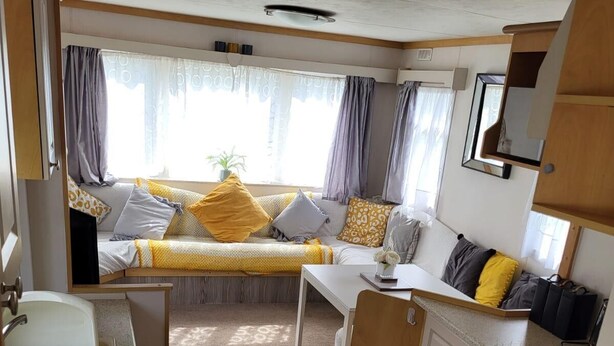 Interior compacto de una caravana, con una kitchenette, zona de estar con cojines y una pequeña mesa.