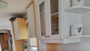 Cocina compacta con armarios blancos, televisor integrado y un refrigerador pequeño.
