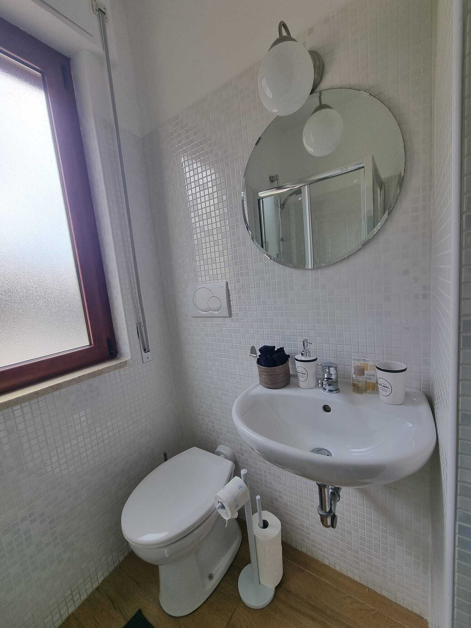 A bathroom with a toilet, sink, mirror, and a window.