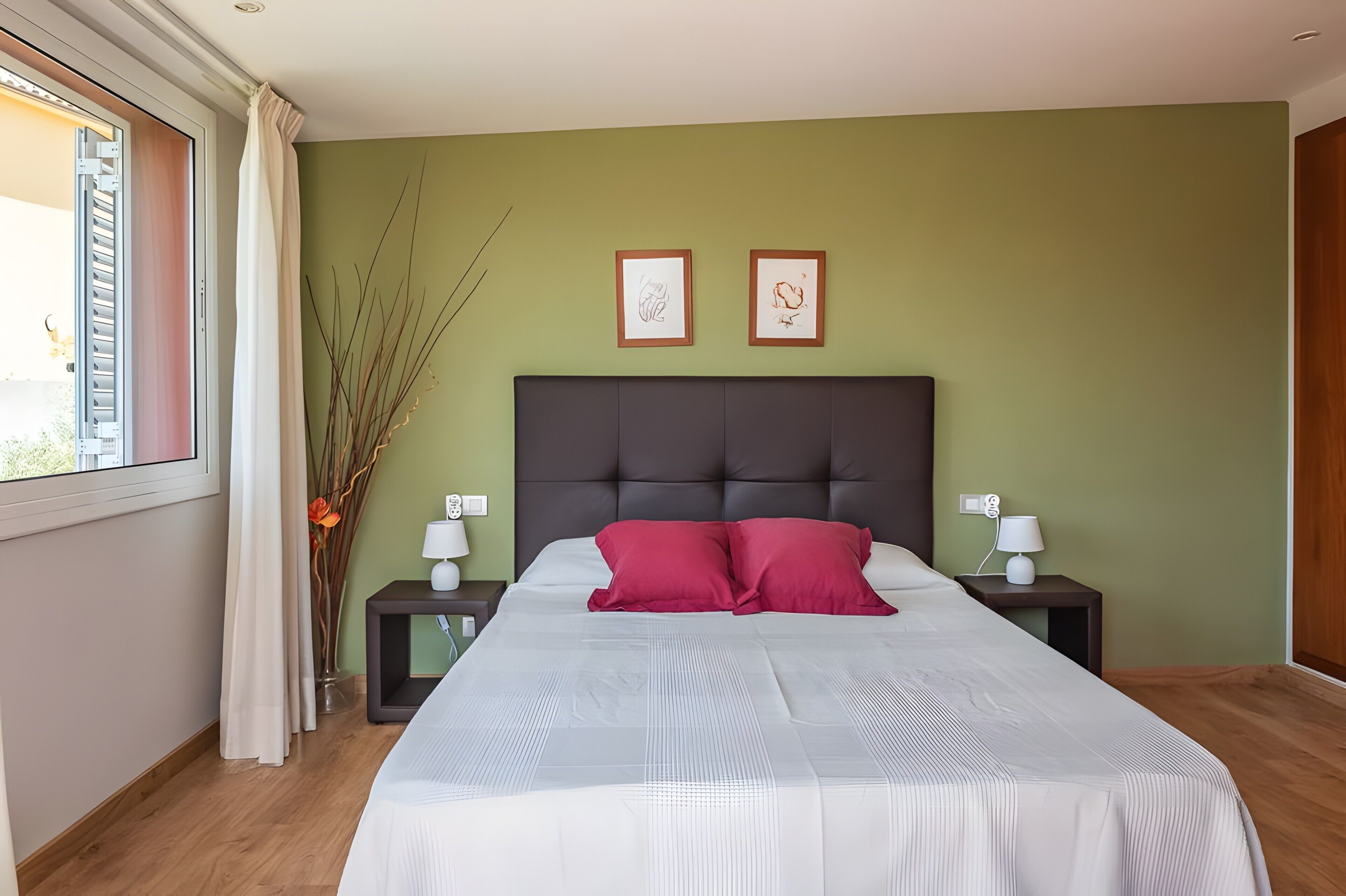 A bedroom with a bed, two nightstands, a window with curtains, and two framed pictures on the wall.