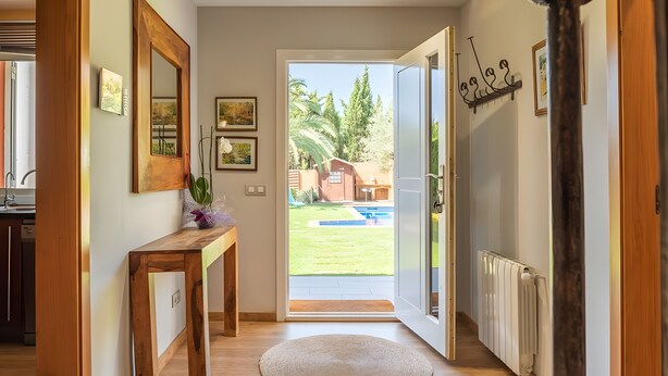 Um corredor com um banco de madeira, um tapete redondo e uma porta que dá para um quintal com piscina.