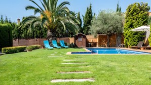 Um quintal com piscina, palmeiras e um deck de madeira com espreguiçadeiras.