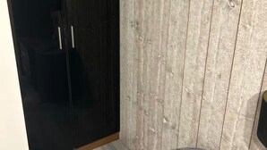 A room with a dark wooden wardrobe, a light wooden wall, and a striped ottoman.