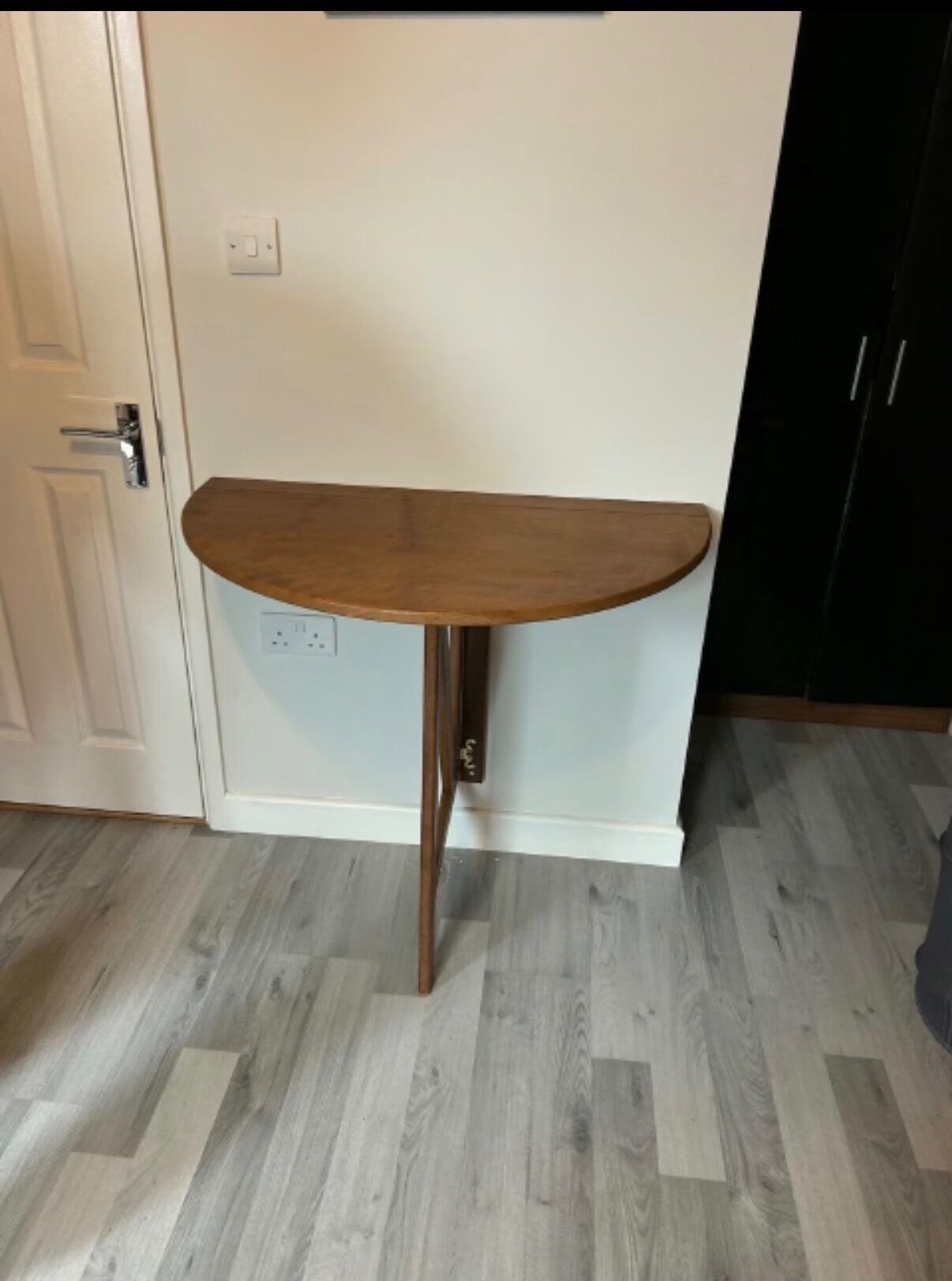 A corner table with a wooden top and metal legs, positioned against a white wall with a door and a black cabinet.