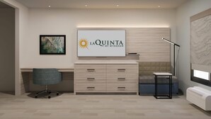 A modern room with a flat-screen TV, a desk, a chair, a sofa, and a lamp. - La Quinta Inn and Suites by Wyndham Torrance Redondo Beach (Inglewood)