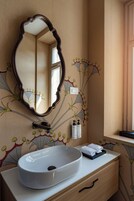 Uma casa de banho com uma pia redonda, um espelho com moldura ornamentada e uma parede com papel de parede floral.