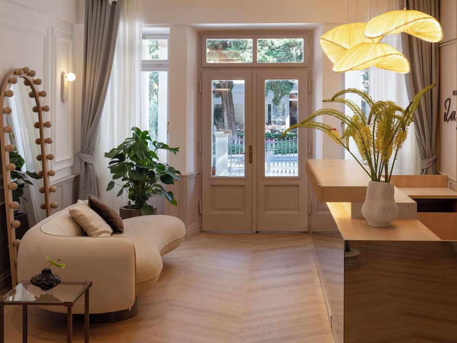 Un vestíbulo de hotel con zona de estar, espejo con iluminación, planta en maceta y mostrador de recepción.