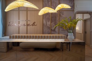 A reception area with a wooden reception desk, a bench, and three hanging lamps. - Heritage Hotel Zagreb Dubrovik (Dubrovnik)