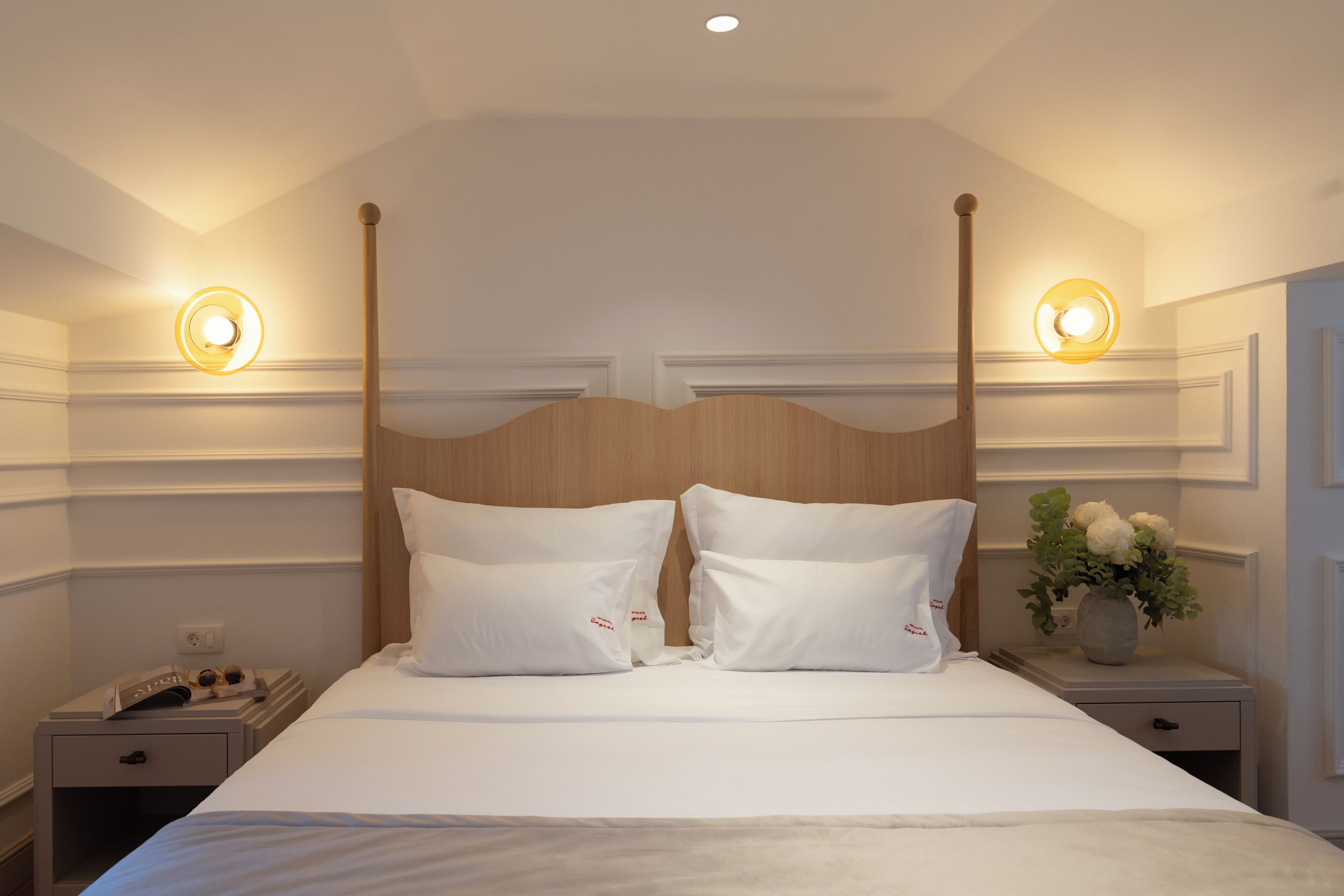 A hotel room with a four-poster bed, two bedside tables, and a nightstand with a lamp.