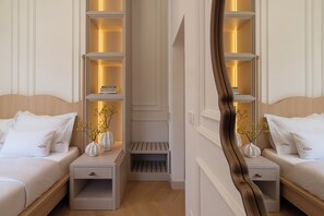 Une chambre d’hôtel avec deux lits, des tables de chevet et une étagère centrale où sont disposés des livres et des objets décoratifs.