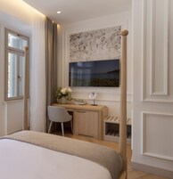Quarto com cama, escrivaninha, cadeira e janela com vista para o mar, e cortina.
