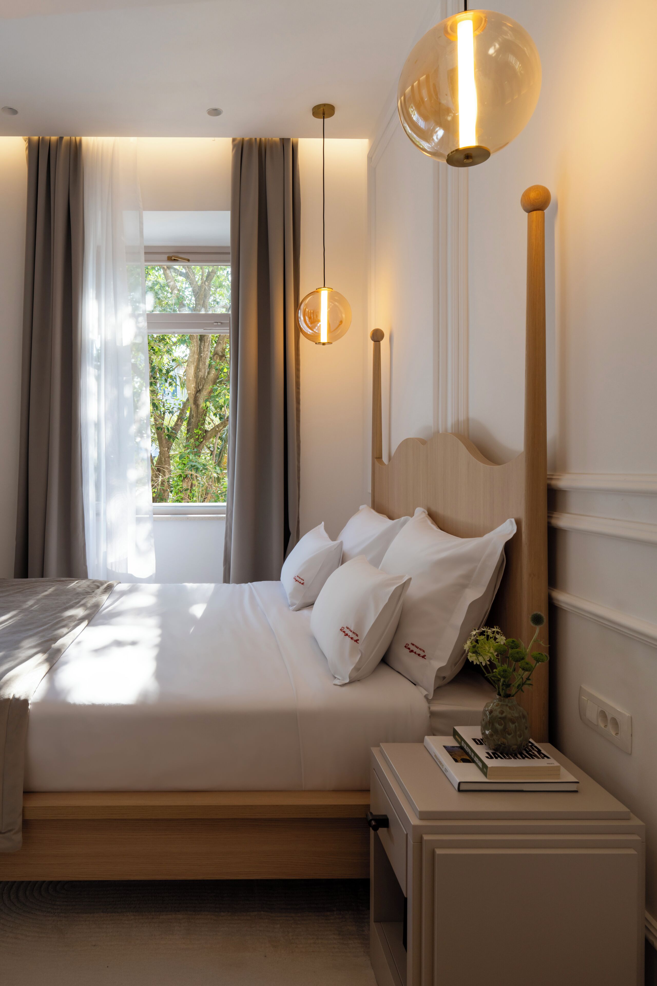 Un dormitorio moderno con una cama grande, una mesita de noche con un libro y un florero, y una ventana con cortinas.
