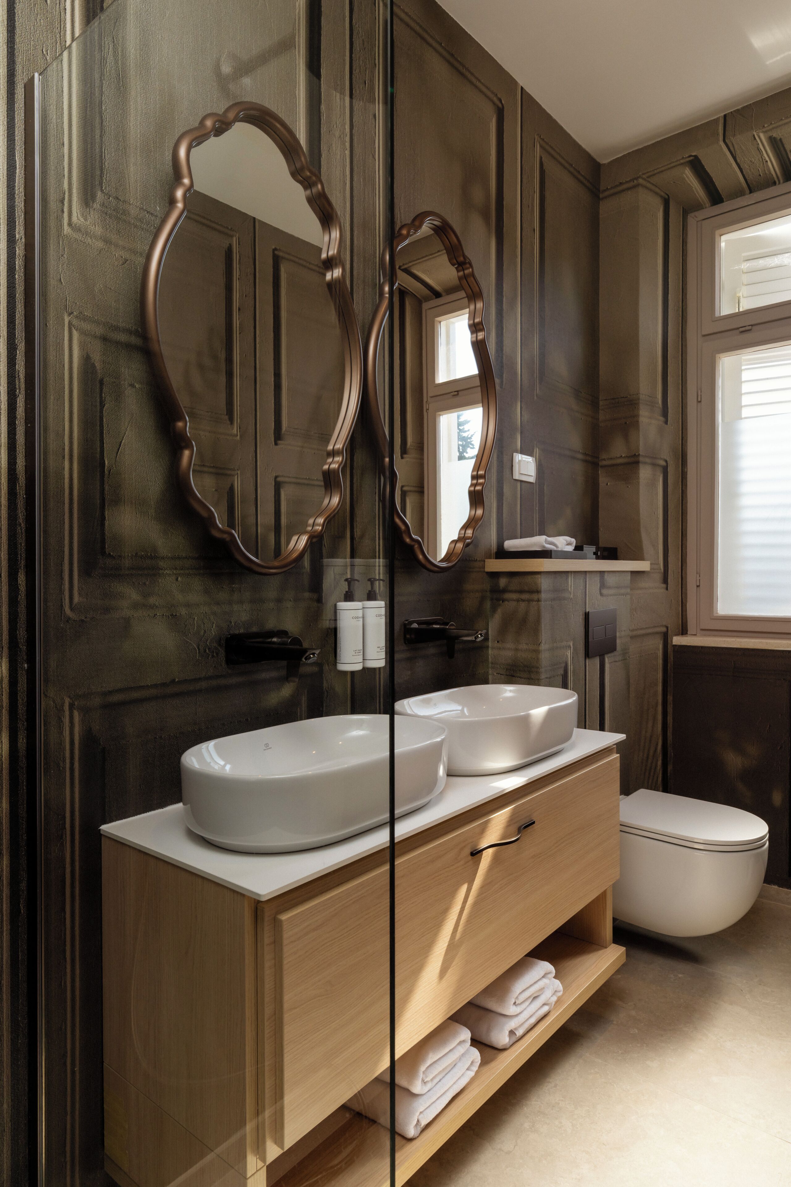 A bathroom with two round mirrors, a white sink, and a toilet.