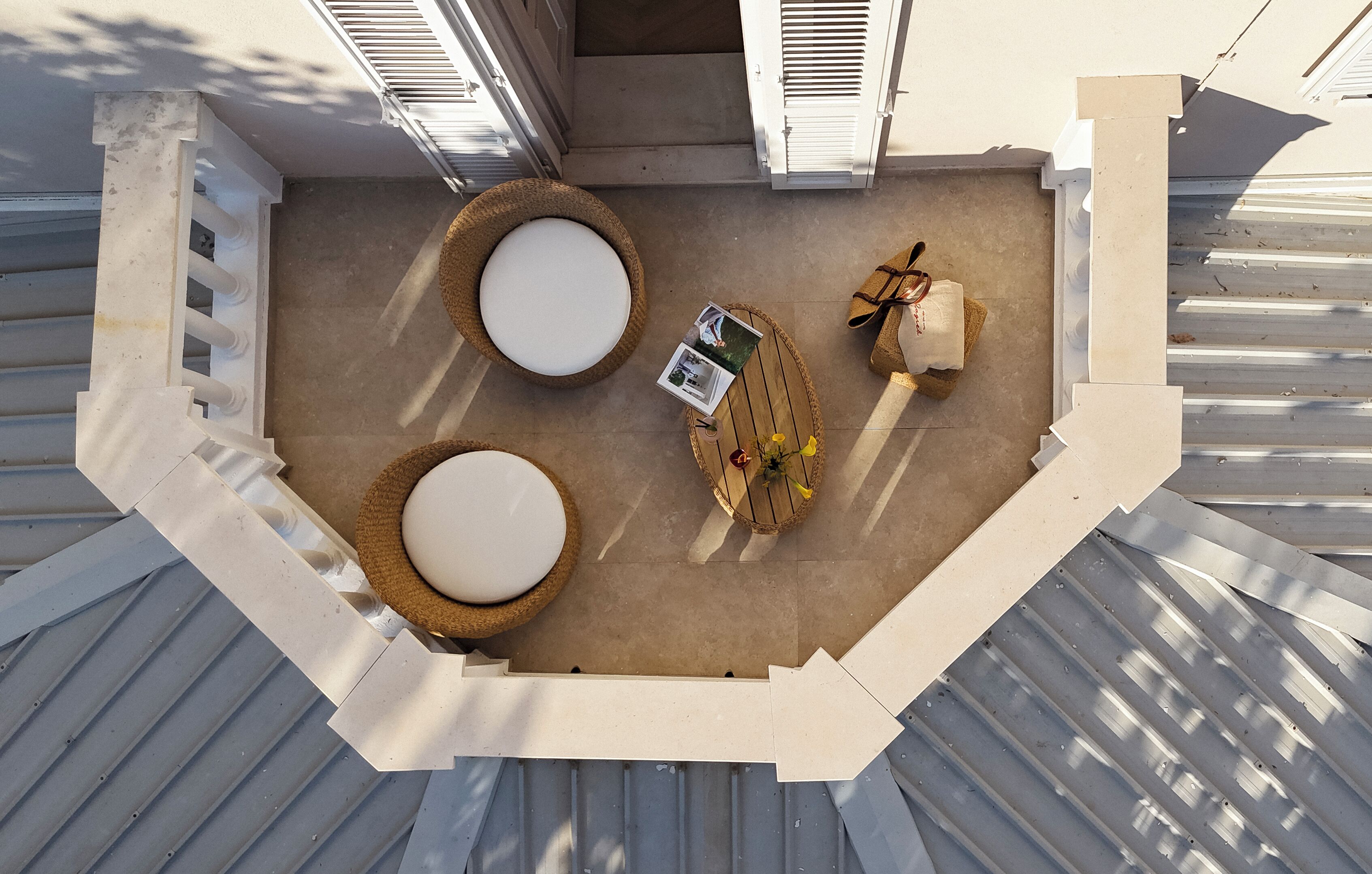 An outdoor seating area with two round tables, a small table with a book and flowers, and a cushioned bench.