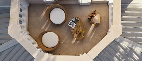 An outdoor seating area with two round tables, a small table with a book and flowers, and a cushioned bench.