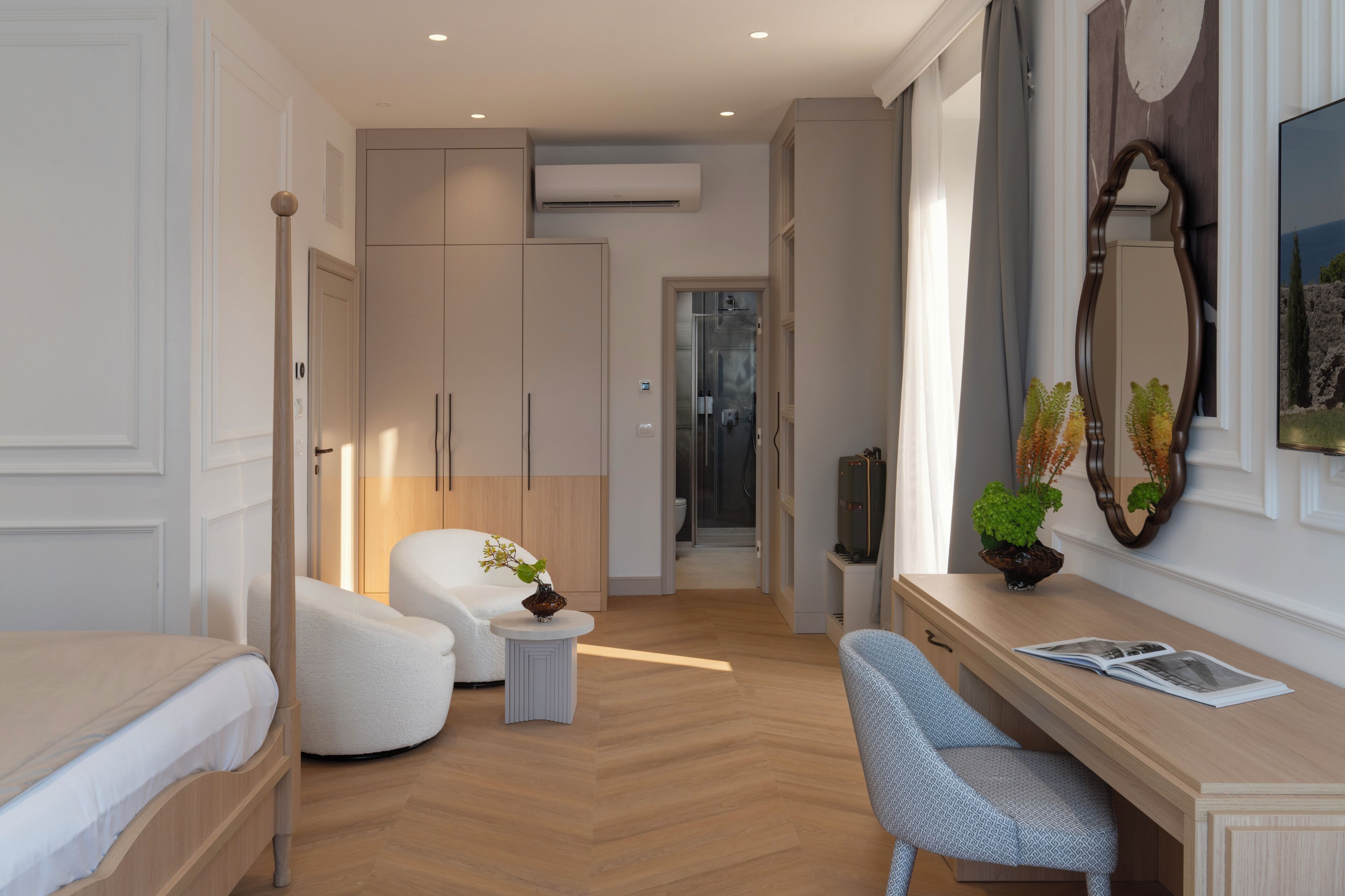 Een moderne hotelkamer met een bed, een zithoek met een stoel en een tafeltje, een kaptafel met spiegel, en een doucheruimte.