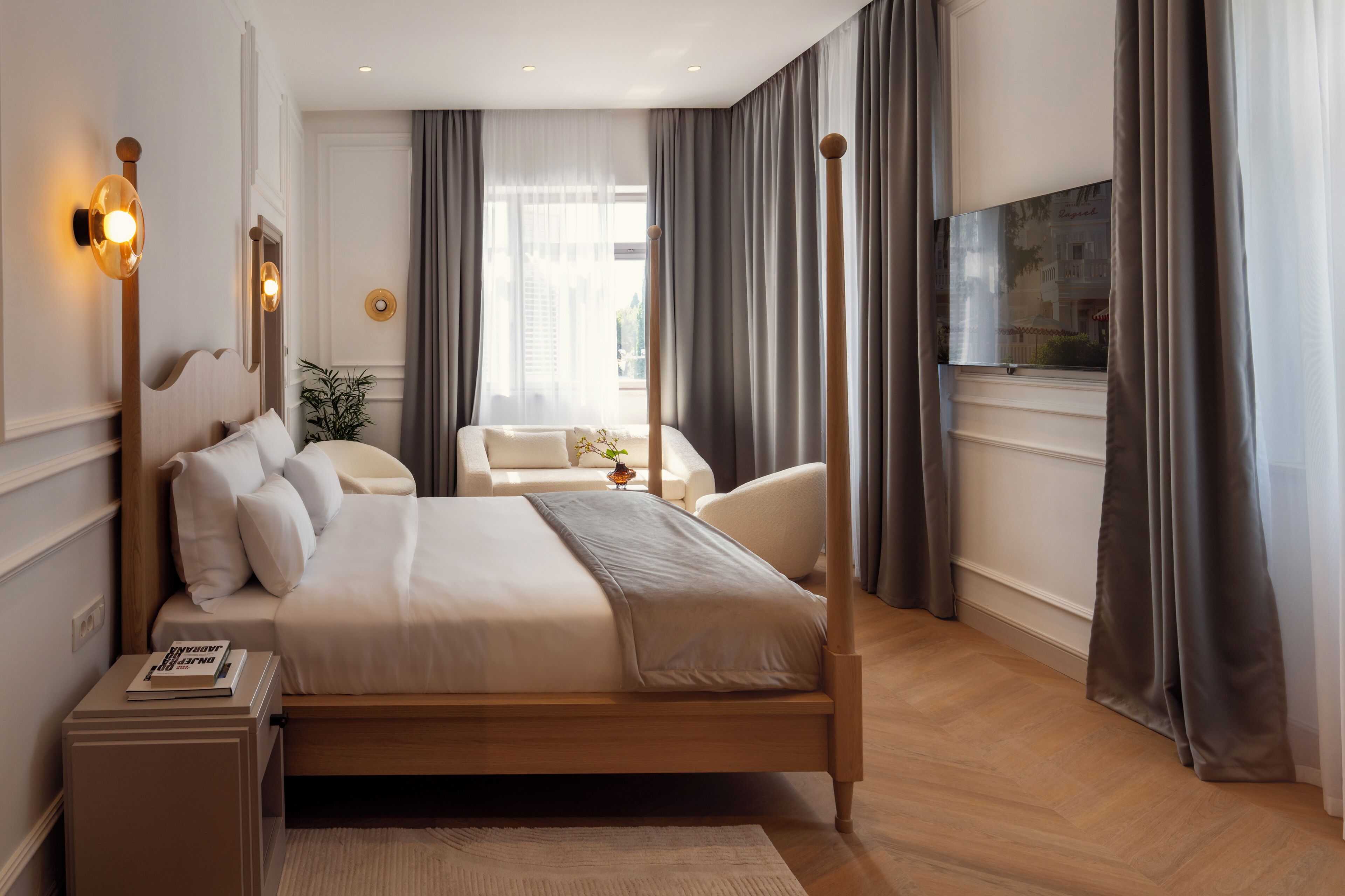 Une chambre d’hôtel moderne avec un grand lit, une table de chevet, une chaise, une petite table avec un vase et un téléviseur fixé au mur.