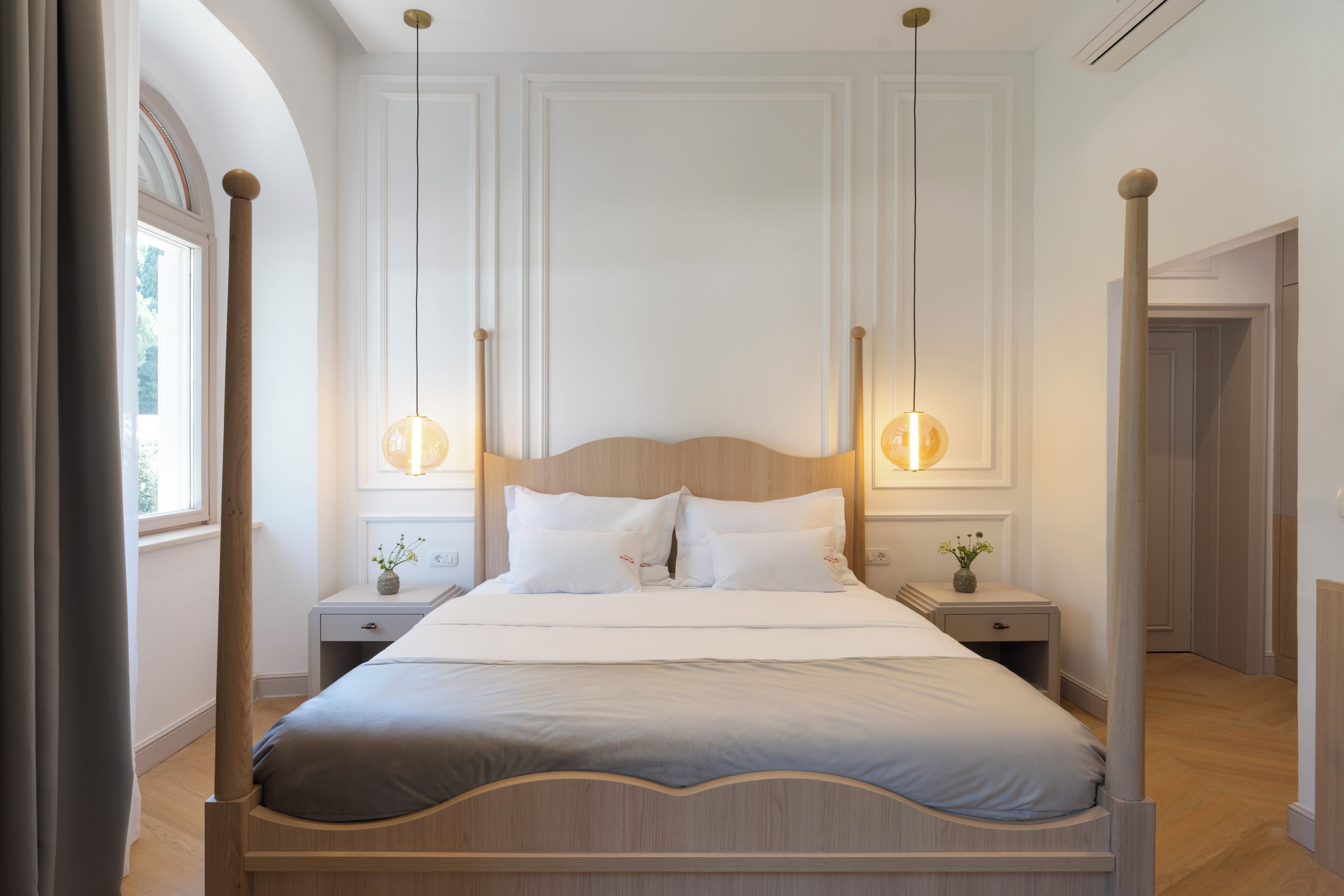 A hotel room with a large bed, two bedside tables, a nightstand, a window with curtains, and a door.