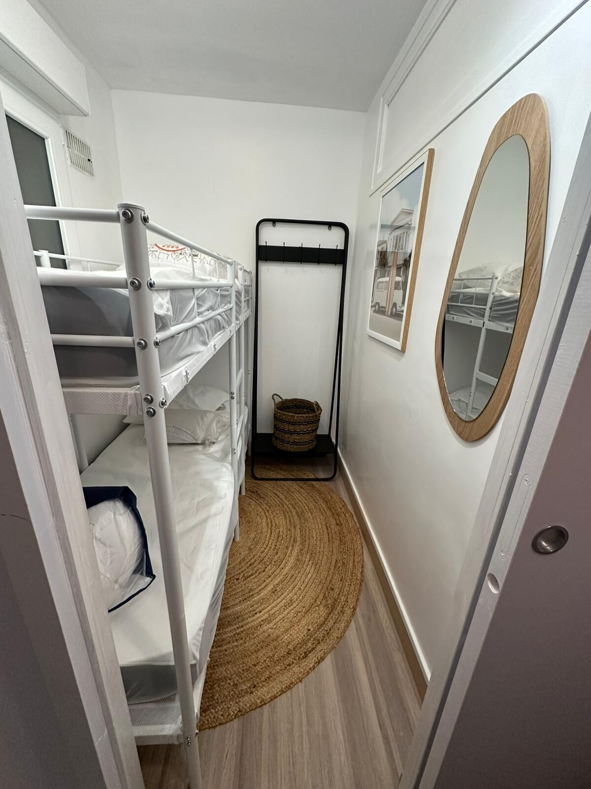 A narrow hallway with bunk beds, a woven rug, a mirror, and a door.