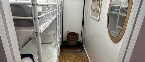 A narrow hallway with bunk beds, a woven rug, a mirror, and a door.