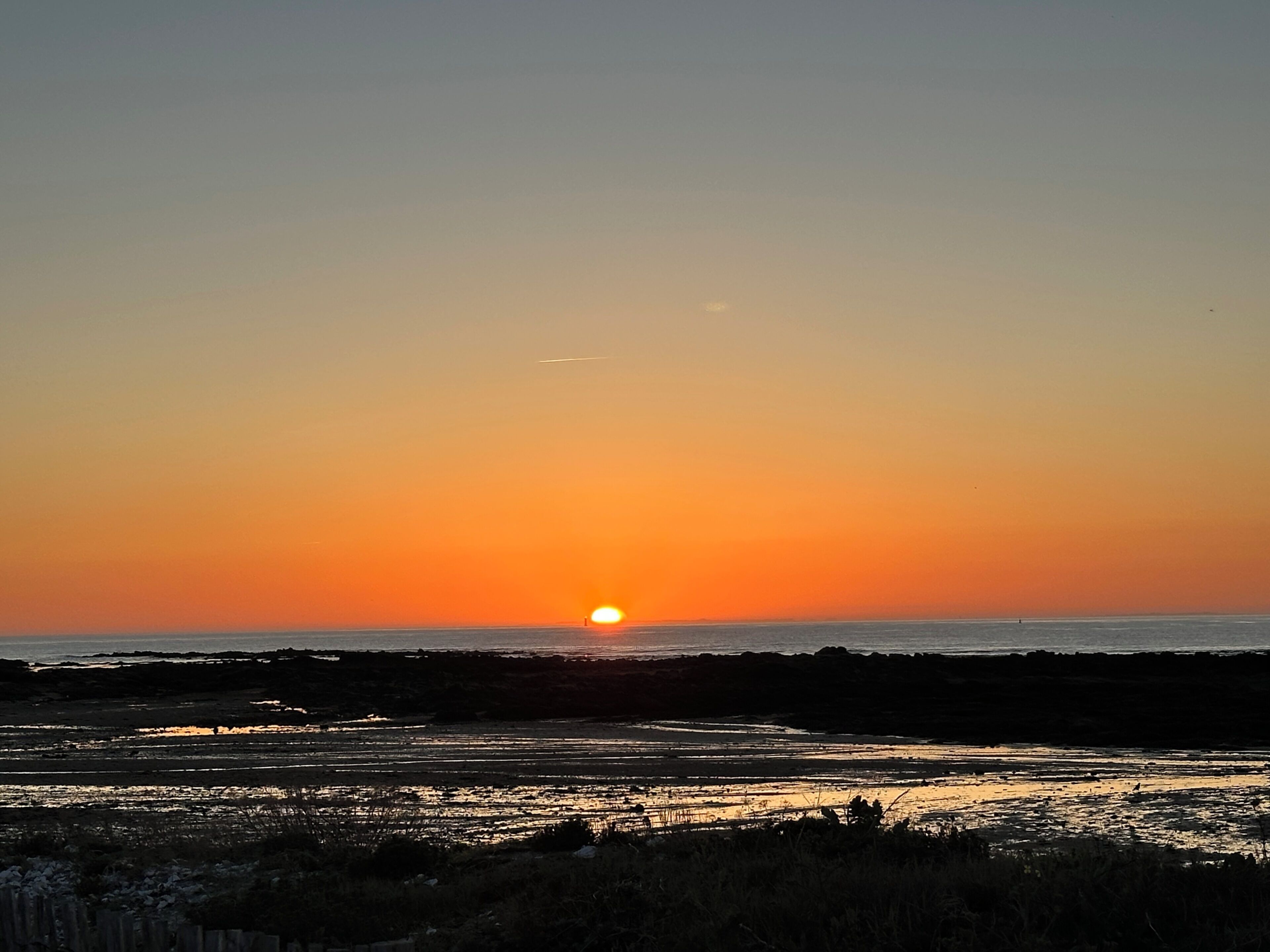 Een zonsondergang boven een strand met een heldere lucht.