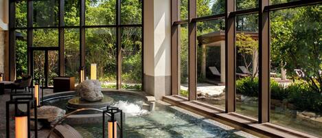 A spa area with a hot tub, large windows, and a view of the surrounding greenery.