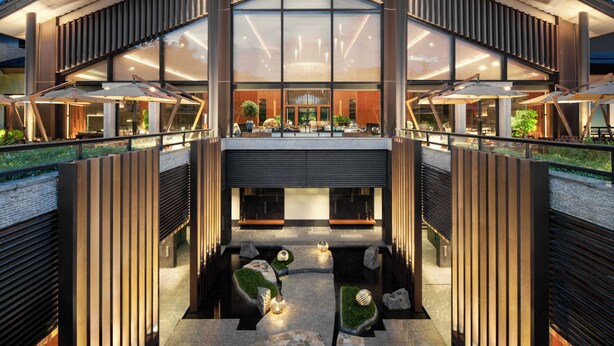 A modern hotel with a central atrium, outdoor seating, and a view of the interior.