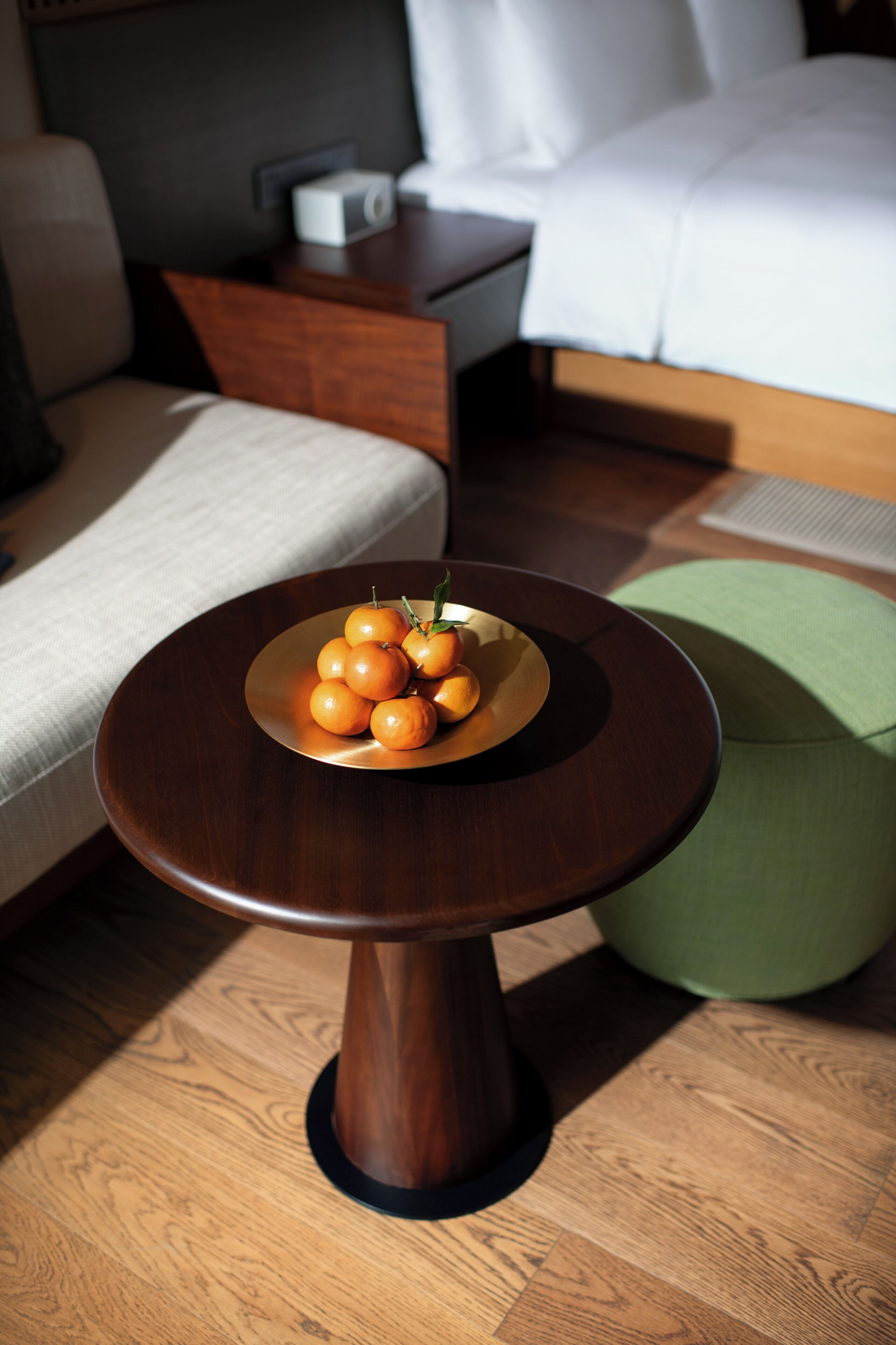 A round wooden table with a plate of oranges in a hotel room.