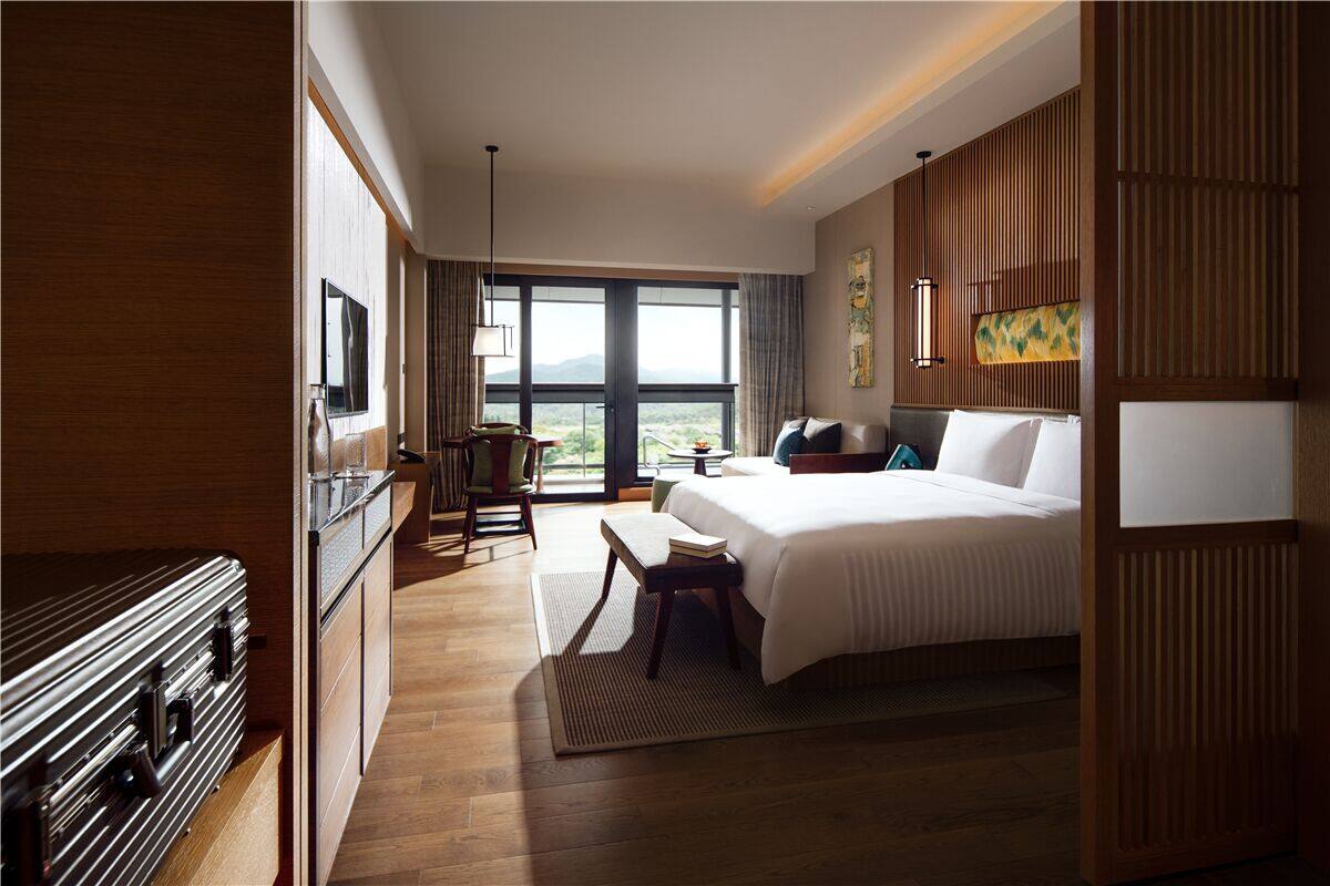 A hotel room with a large bed, a desk, a chair, a TV, and a view of the outdoors.