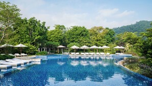 A swimming pool with lounge chairs and umbrellas, surrounded by lush greenery and hills.