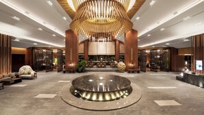 A spacious lobby with a central circular fountain, wooden accents, and modern lighting.