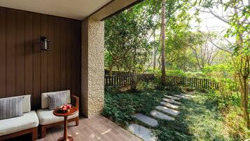 A covered patio with a sofa, a small table with fruit, and a stone pathway leading to a garden.