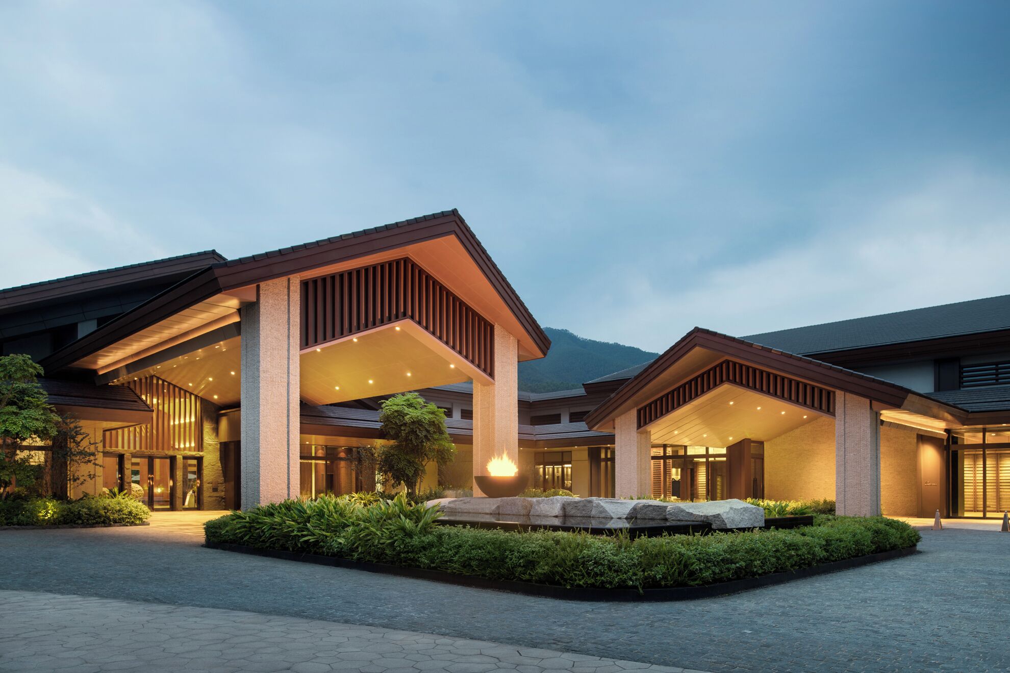 A modern hotel with a covered entrance, outdoor seating area, and a landscaped garden.