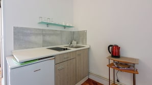 Eine kleine Küche mit einem weißen Kühlschrank, Holzschränken, einem Spülbecken und einem Wasserkocher auf einem Tisch.