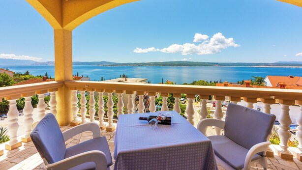 Ein Balkon mit Tisch und Stühlen, der Blick auf die Küste freigibt.
