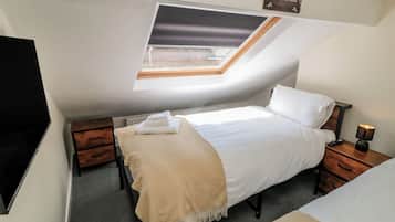 A bedroom with a skylight, a bed, a bedside table with a lamp, and a TV on the wall.