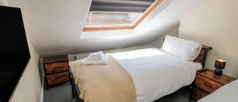 A bedroom with a skylight, a bed, a bedside table with a lamp, and a TV on the wall.