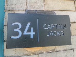 Ein schwarzes Schild mit der Nummer 34 und dem Schriftzug 'CAPTAIN JACKS' an einer Steinmauer.